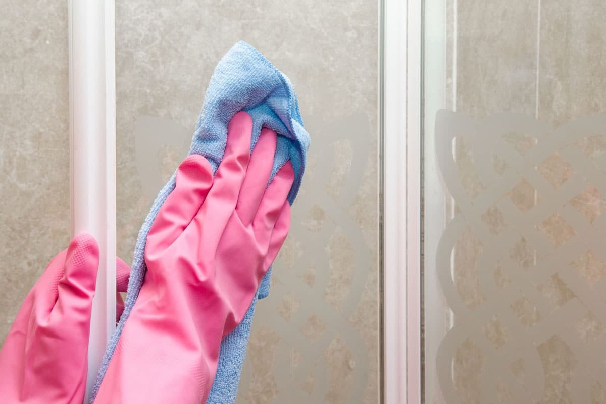 A pink-gloved hand wiping a shower glass door