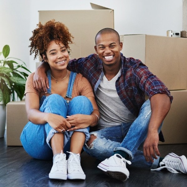 A smiling couple sitting among moving boxes in their new home