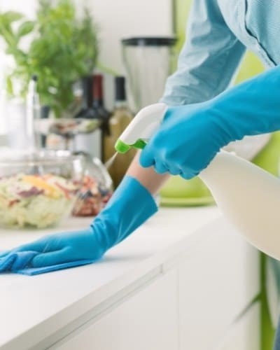A cleaner in blue gloves wiping a kitchen countertop